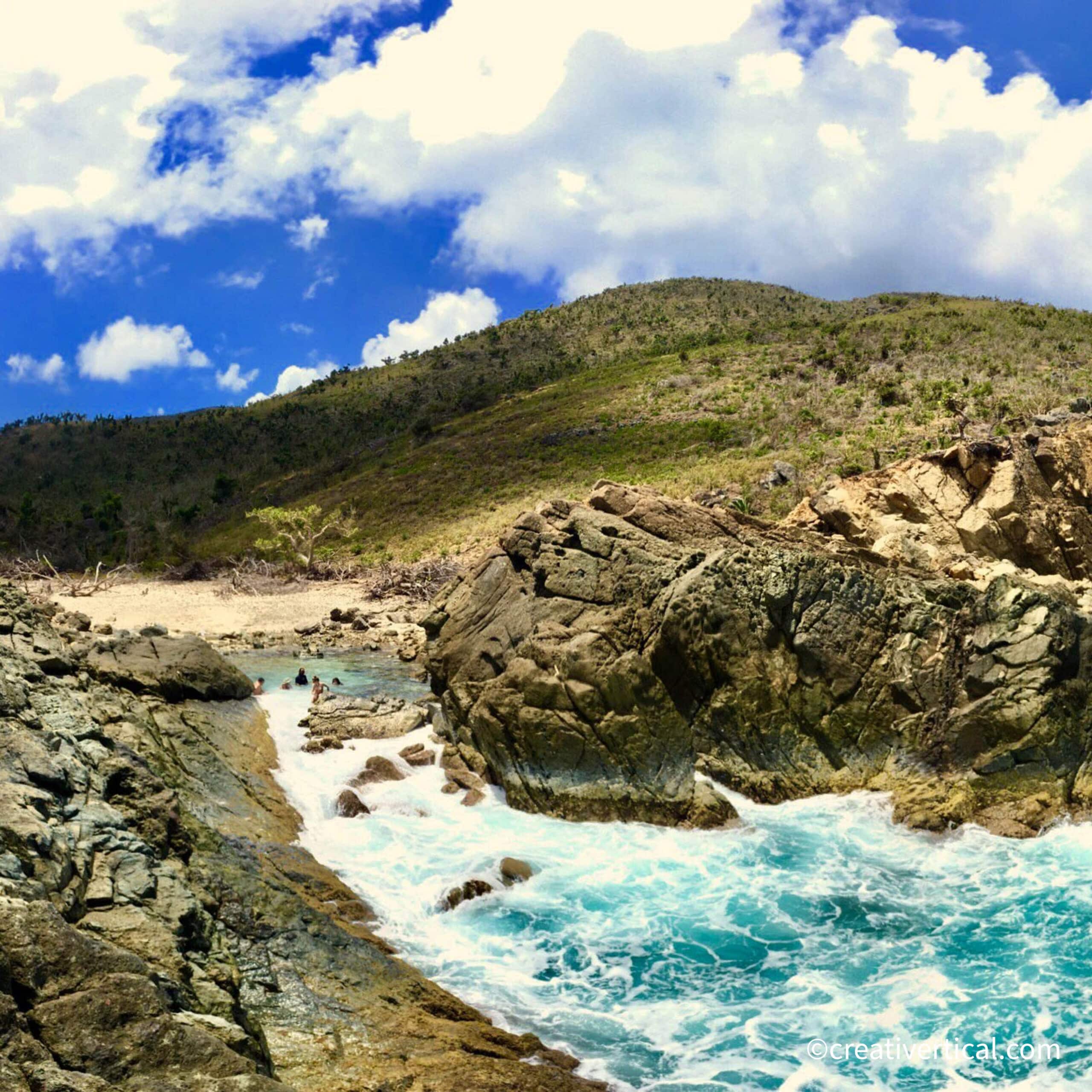Small group of tourists wading in Bubbly Pool at Jost Van Dyke, BVI as winter swell rolls in.